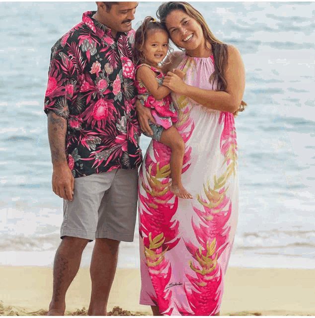 a woman in a pink dress holds a little girl while standing next to a man in a floral shirt