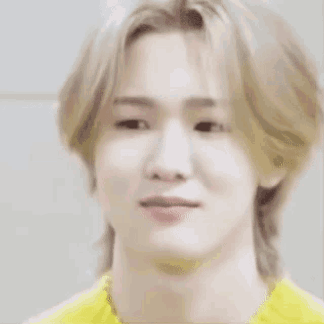 a close up of a young man with blonde hair wearing a yellow shirt .