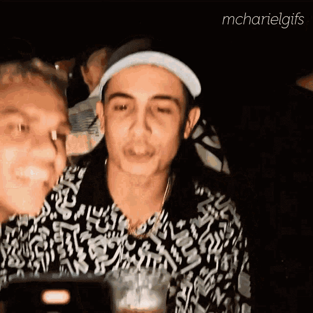 a man in a hat is talking to another man in a black and white shirt
