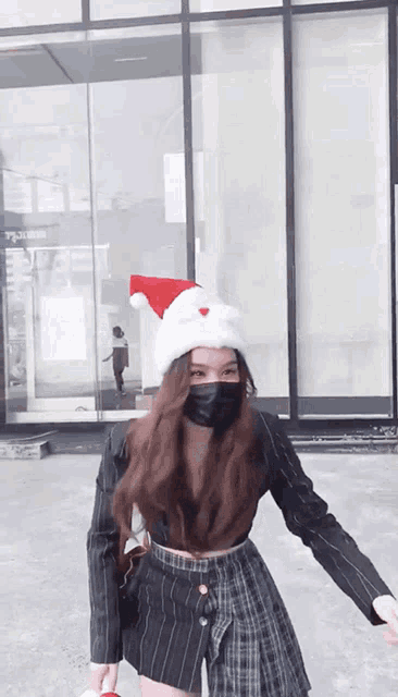 a woman wearing a santa hat and a mask stands in front of a building