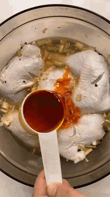 a measuring spoon is being used to pour sauce into a bowl of chicken