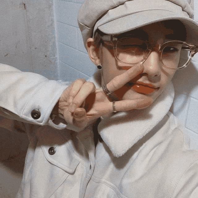 a person wearing glasses and a hat is giving the peace sign