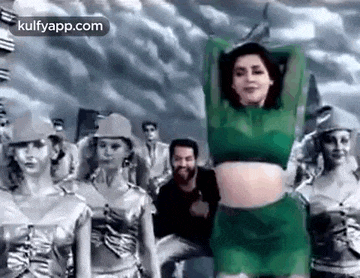 a woman in a green crop top and shorts is dancing in front of a group of people .