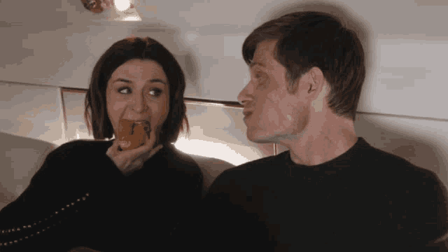 a man and a woman are sitting next to each other and the woman is eating something