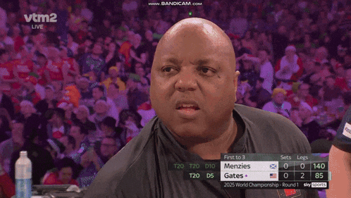 a bald man is holding a dart in his hand while watching a match on vtm2