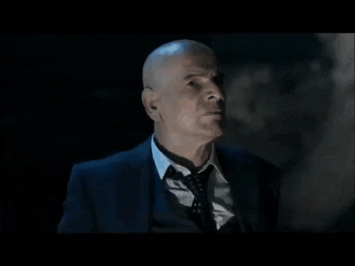 a man in a suit is pointing a gun at another man in a chair