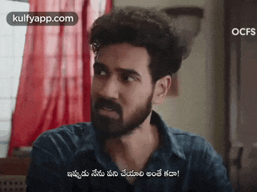 a man with a beard is talking to another man in a room with a red curtain behind him .
