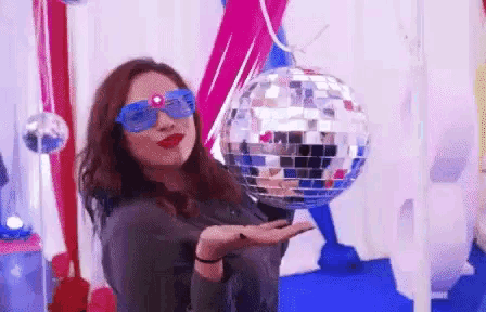 a woman is holding a disco ball in her hand while wearing sunglasses .