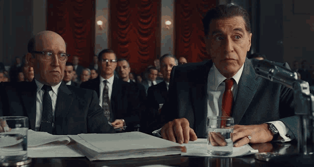 a man in a suit sits in front of a microphone