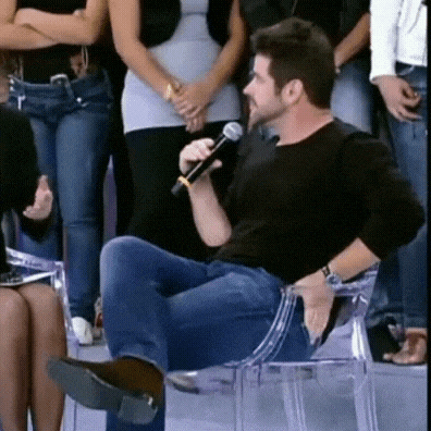 a man in a black shirt is sitting on a clear chair holding a microphone