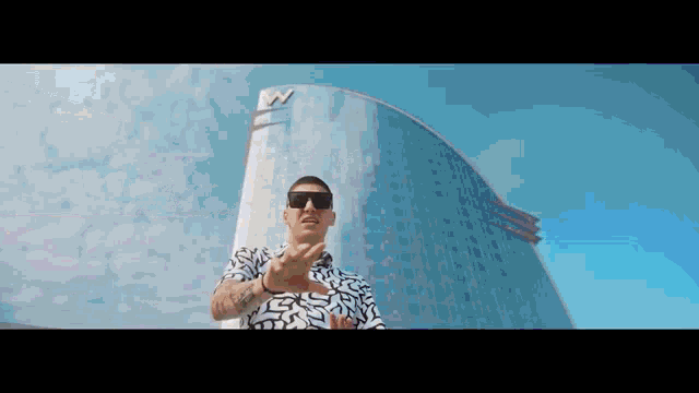 a man wearing sunglasses stands in front of a tall building
