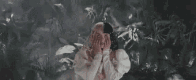 a woman in a white hoodie is covering her face with her hands in a dark room .
