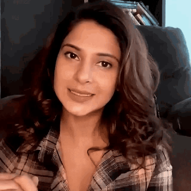 a woman in a plaid shirt sits in a chair and smiles