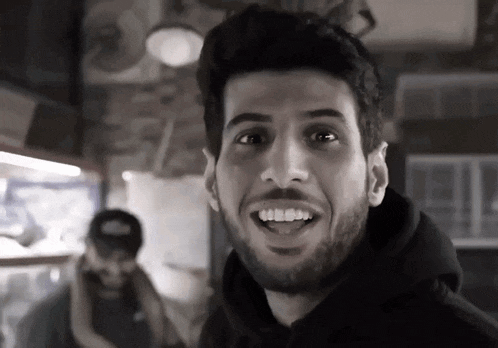 a man with a beard wearing a black hoodie smiles for the camera