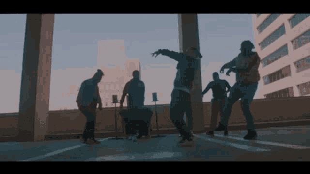 a group of men are dancing on a rooftop in front of a building