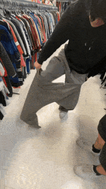 a man is trying on a pair of grey pants in a clothing store