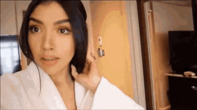 a woman in a white robe is standing in front of a door and holding her hair .