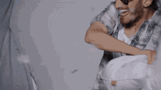 two men are having a pillow fight and one of them is wearing sunglasses