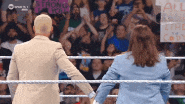 a man and a woman are shaking hands in a wrestling ring while a crowd watches .