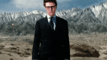 a man in a suit and tie is standing in front of a mountain