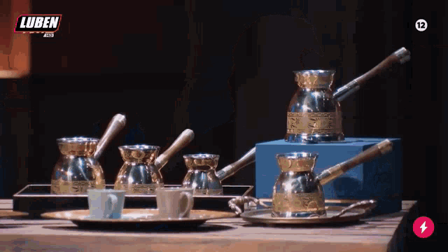 a row of coffee pots and cups on a table with a luben logo behind them