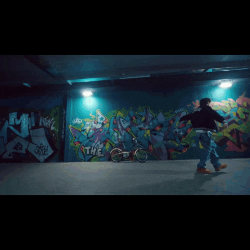 a person riding a bike in front of a wall with graffiti that says the