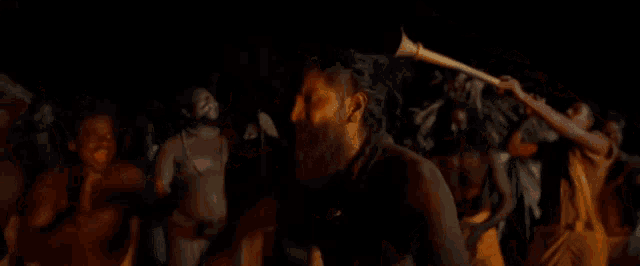 a man with a beard is standing in a crowd of people holding a stick