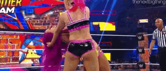 two women are wrestling in a wrestling ring with a referee watching .