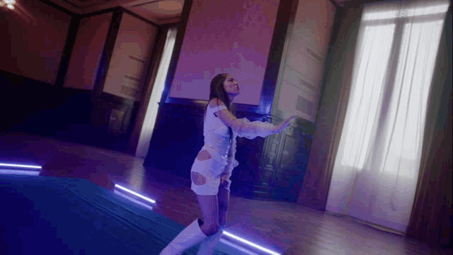 a woman in a white dress and white boots is dancing in a dark room