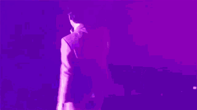 a man in a suit is standing on a stage in front of a microphone in a purple light .