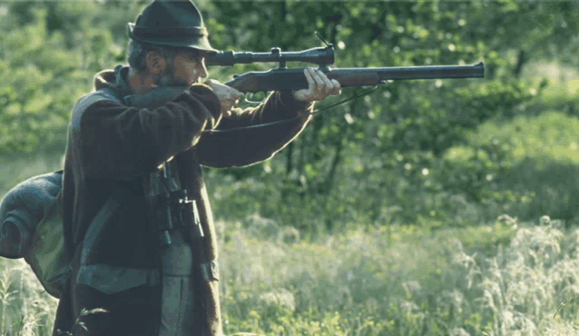 a man in a hat is aiming a rifle