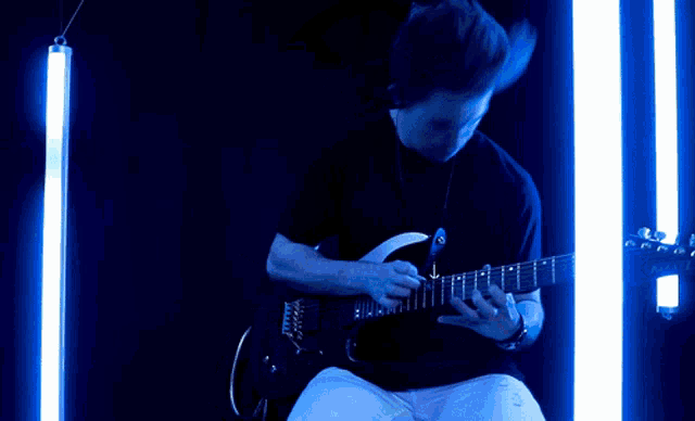 a man is playing a guitar in a dark room with blue lights behind him