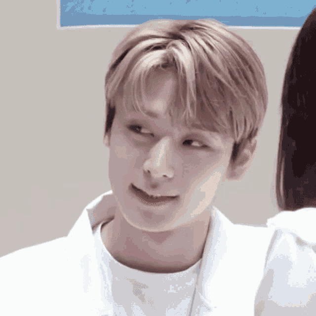 a close up of a young man with blonde hair making a funny face while standing next to a woman .