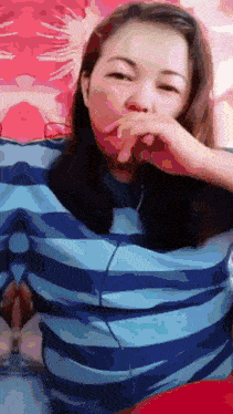 a woman wearing a blue and white striped shirt covering her mouth