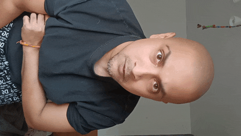 a man with a shaved head wears a black shirt that says dc on it