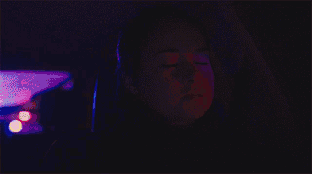 a woman is sitting in a dark room with a pink light behind her