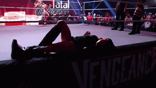 a woman is laying on the floor in a wrestling ring with a sign that says vengeance in the background