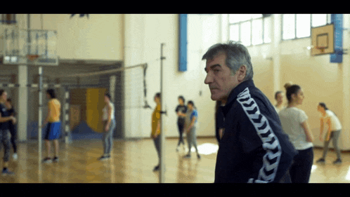 a man wearing a kappa jacket is standing in a gym
