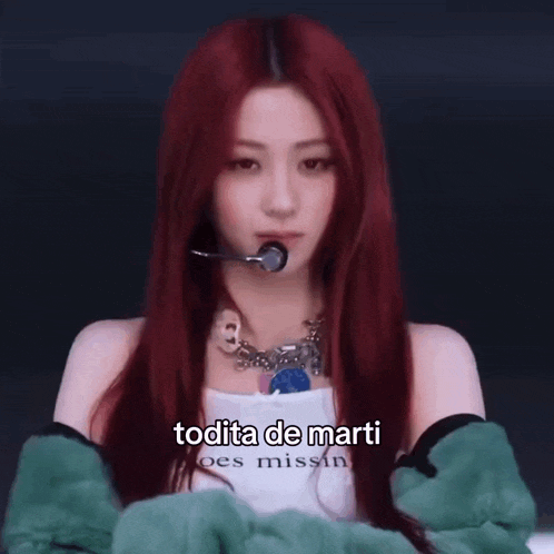 a woman with red hair is wearing a green jacket and a white tank top with the words todita de marti on it .