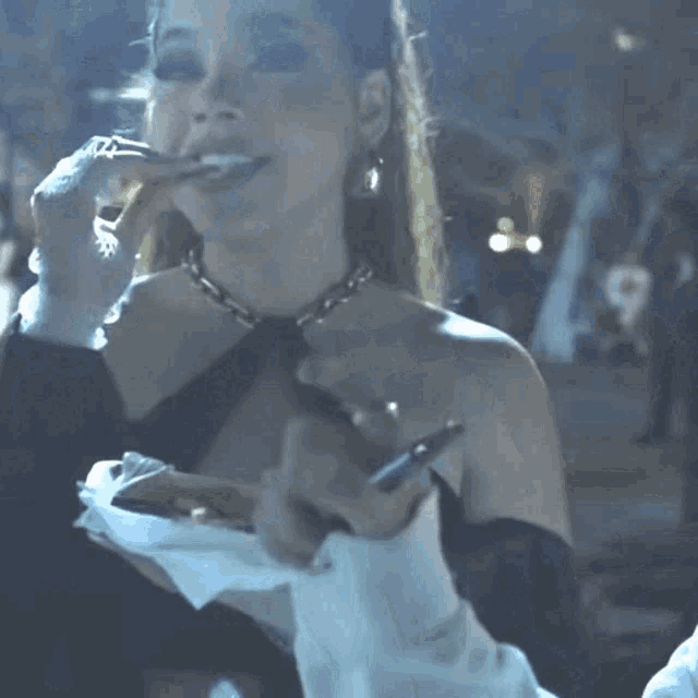 a woman in a black off the shoulder top is holding a cigarette in her hand