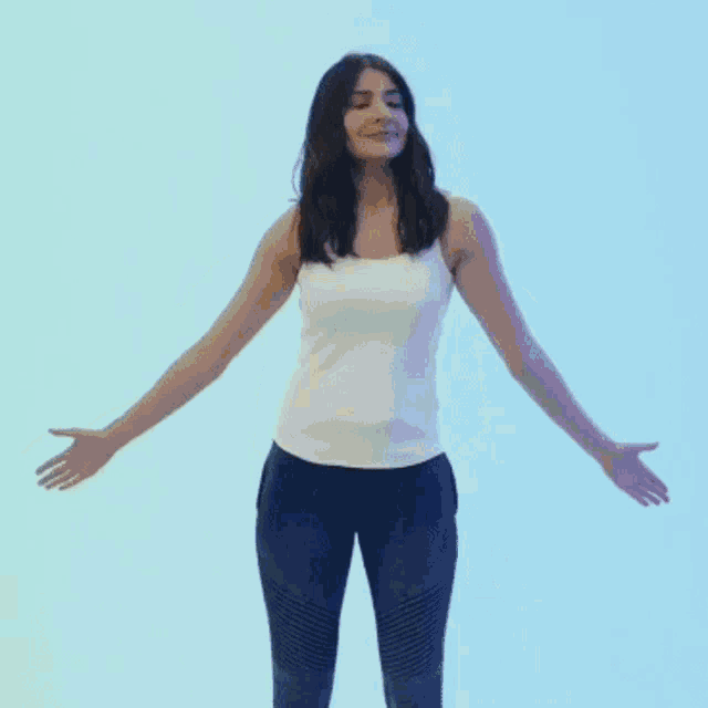 a woman wearing a white tank top and blue jeans is taking off a yellow jacket .