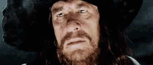 a close up of a man with a beard wearing a hat and looking at the camera .
