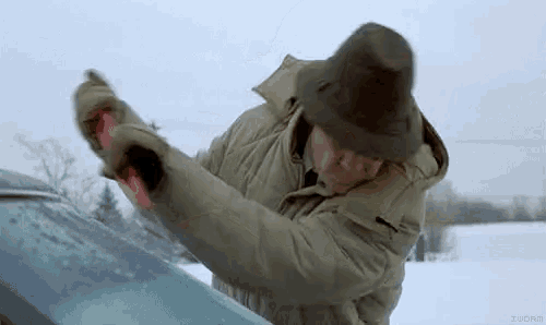a man wearing a hat is cleaning the windshield of a car .