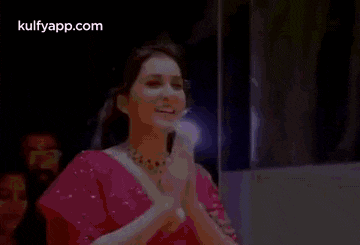 a woman in a pink top is clapping her hands in a room .