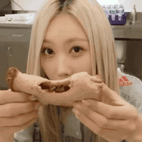 a woman with blonde hair is holding a piece of food in her mouth .
