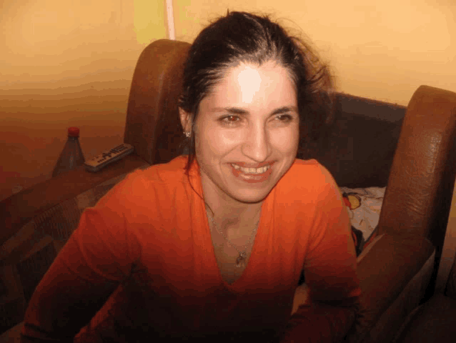 a woman in an orange shirt sits in a chair smiling