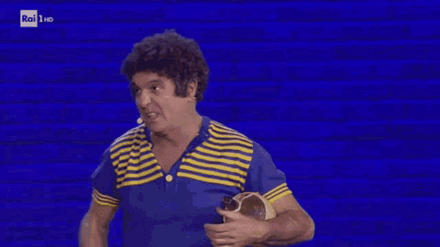 a man in a blue and yellow striped shirt is holding a microphone and making a funny face