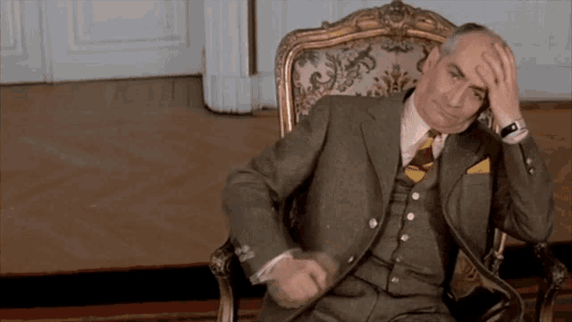 a man in a suit is sitting in a chair with his hand on his forehead