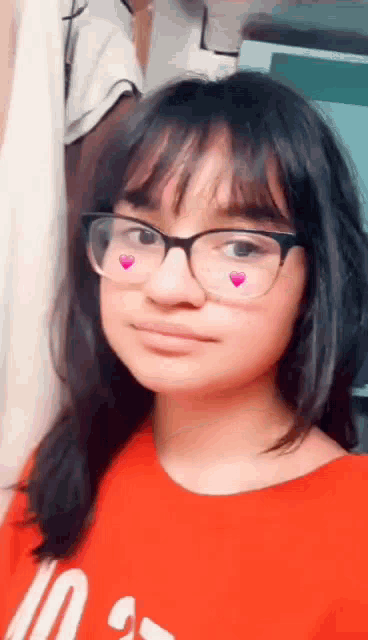 a girl wearing glasses and a red shirt is taking a selfie .