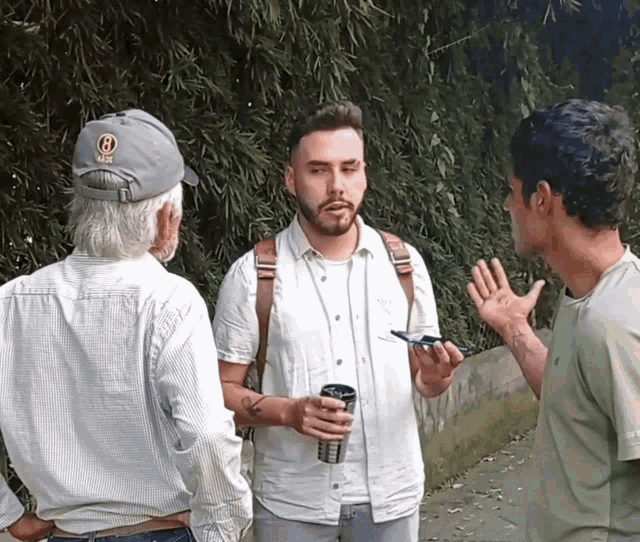 a man wearing a hat with the letter b on it is talking to two other men